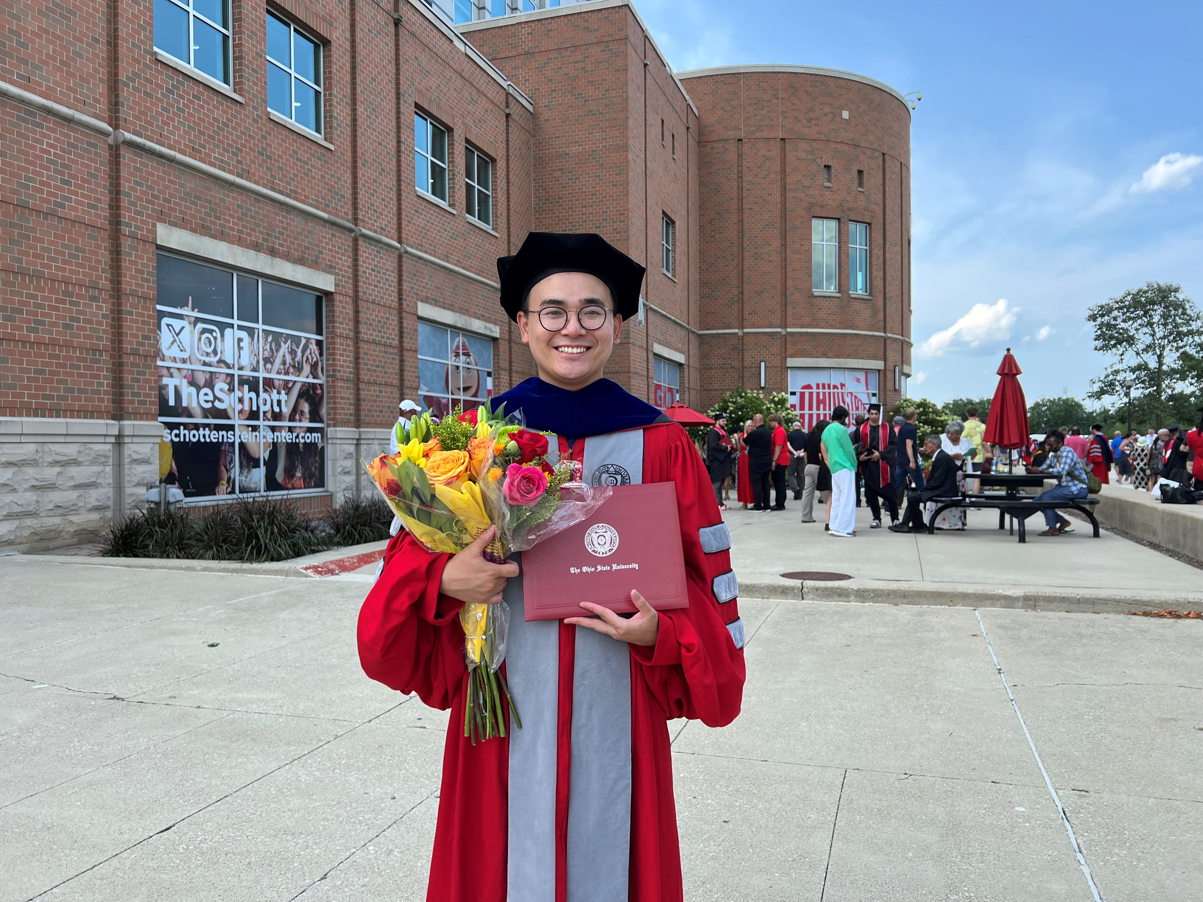 Yifan Li in cap and gown for PhD graduation ceremony at OSU - holding flowers and diploma