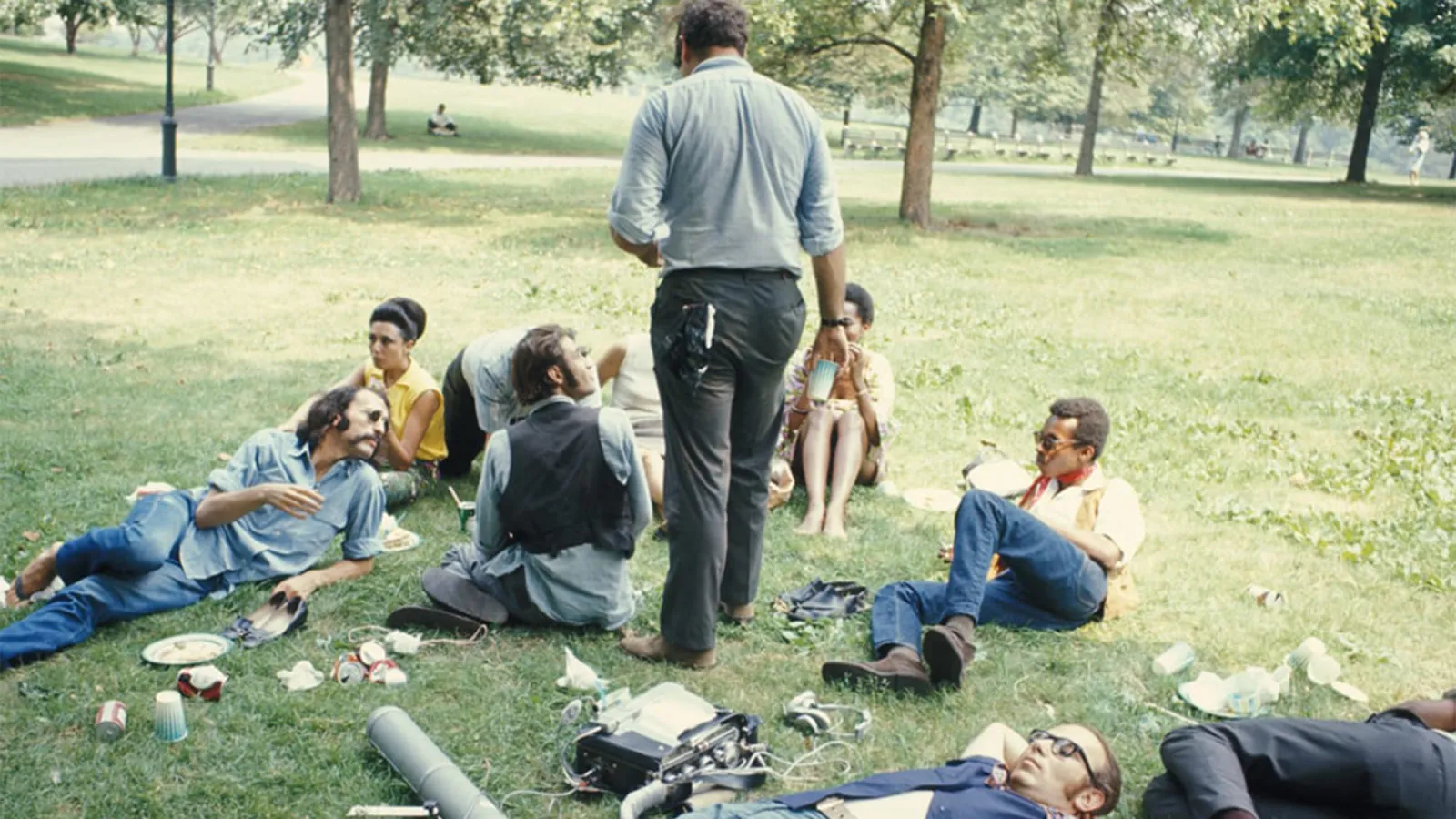 Film still showing group of people sitting talking in grassy field