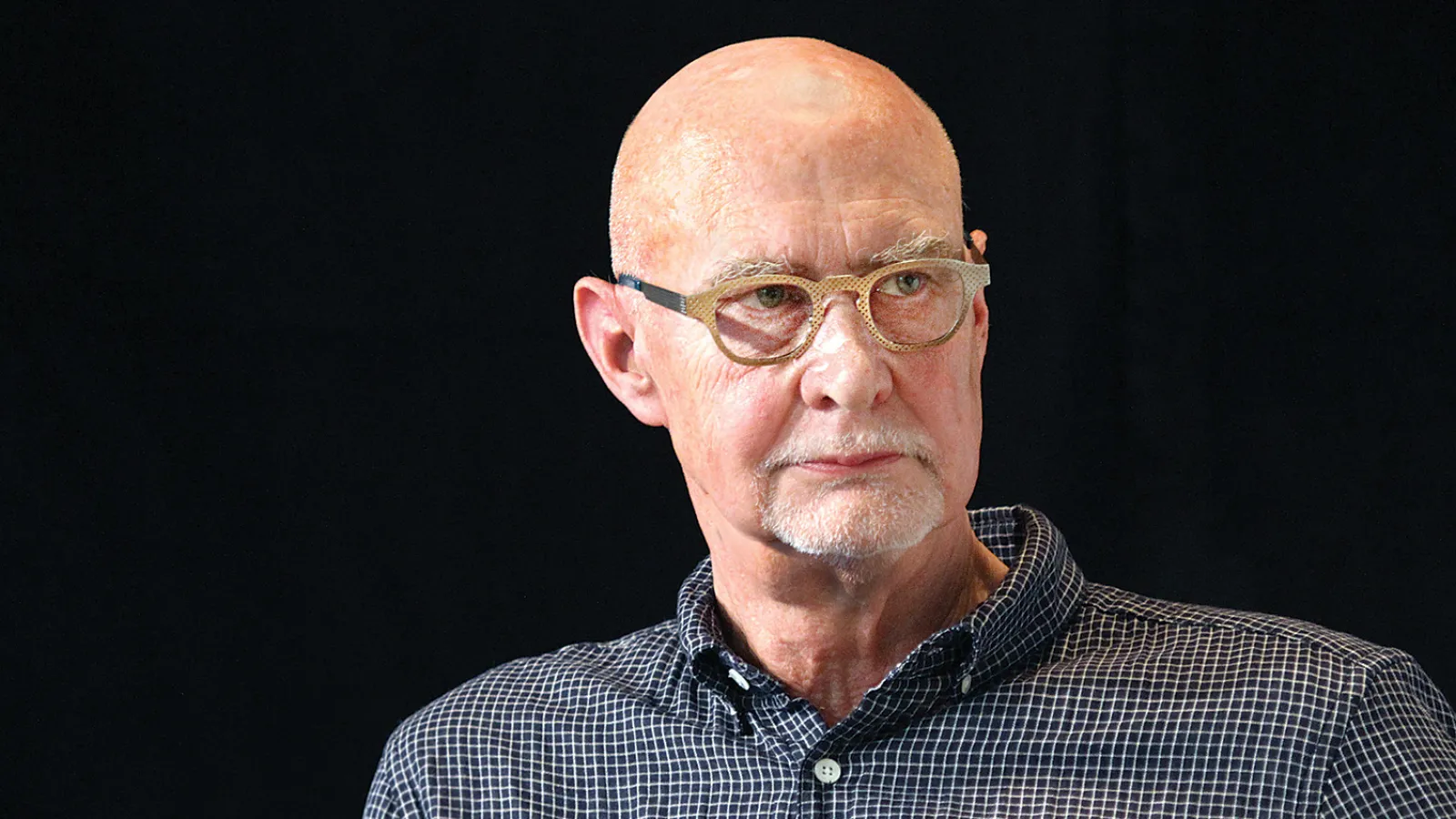 headshot of man with glasses and short white beard on black background