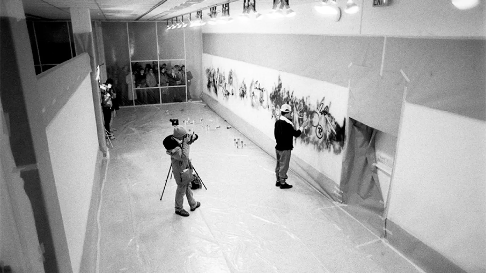 black and white image of a gallery where artist is being filmed