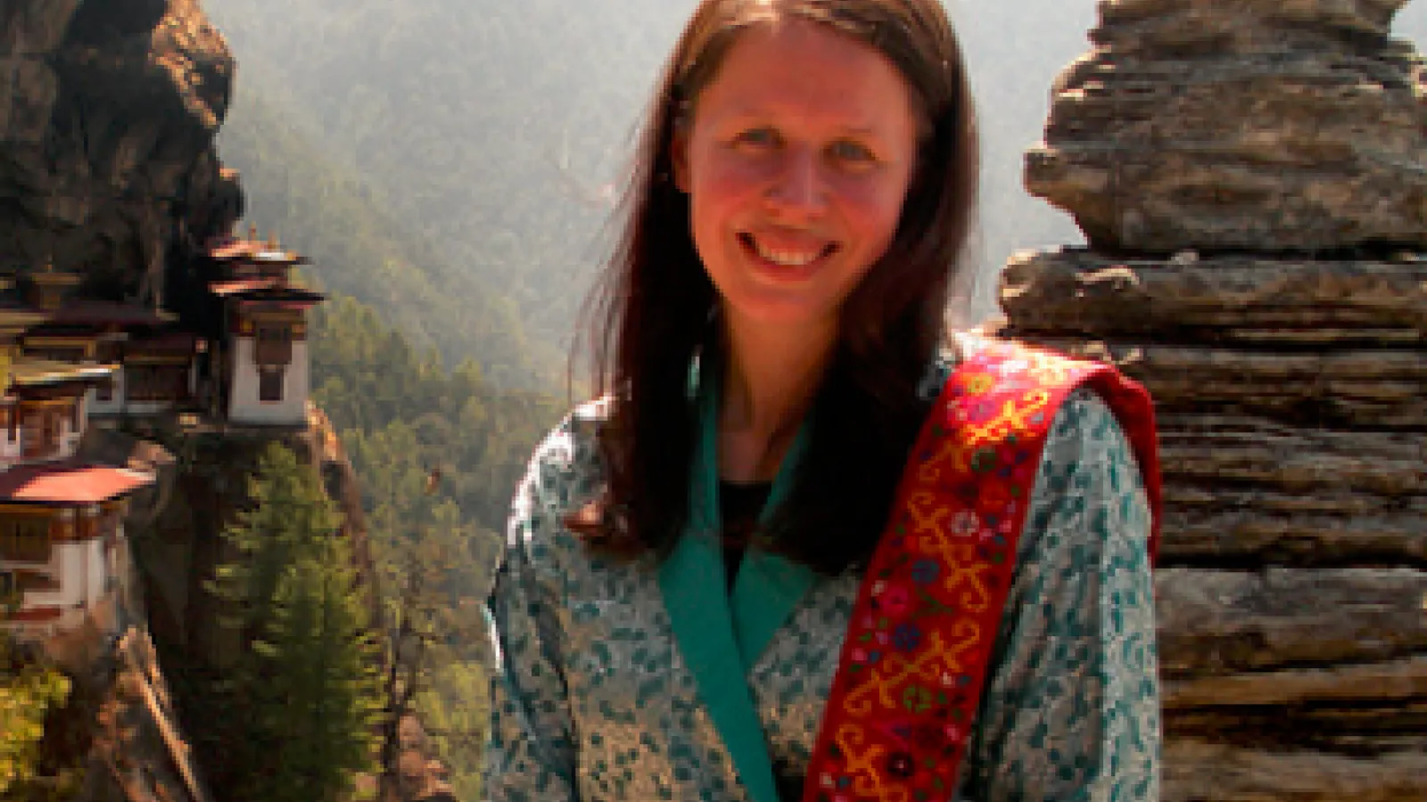 woman with should-length brown hair, light skin, in front of rock formation and mountain