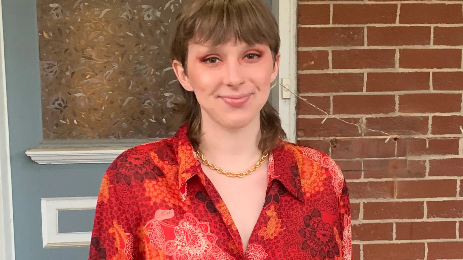 Laurel Hilliard headshot, posing in red shirt in front of brick wall 