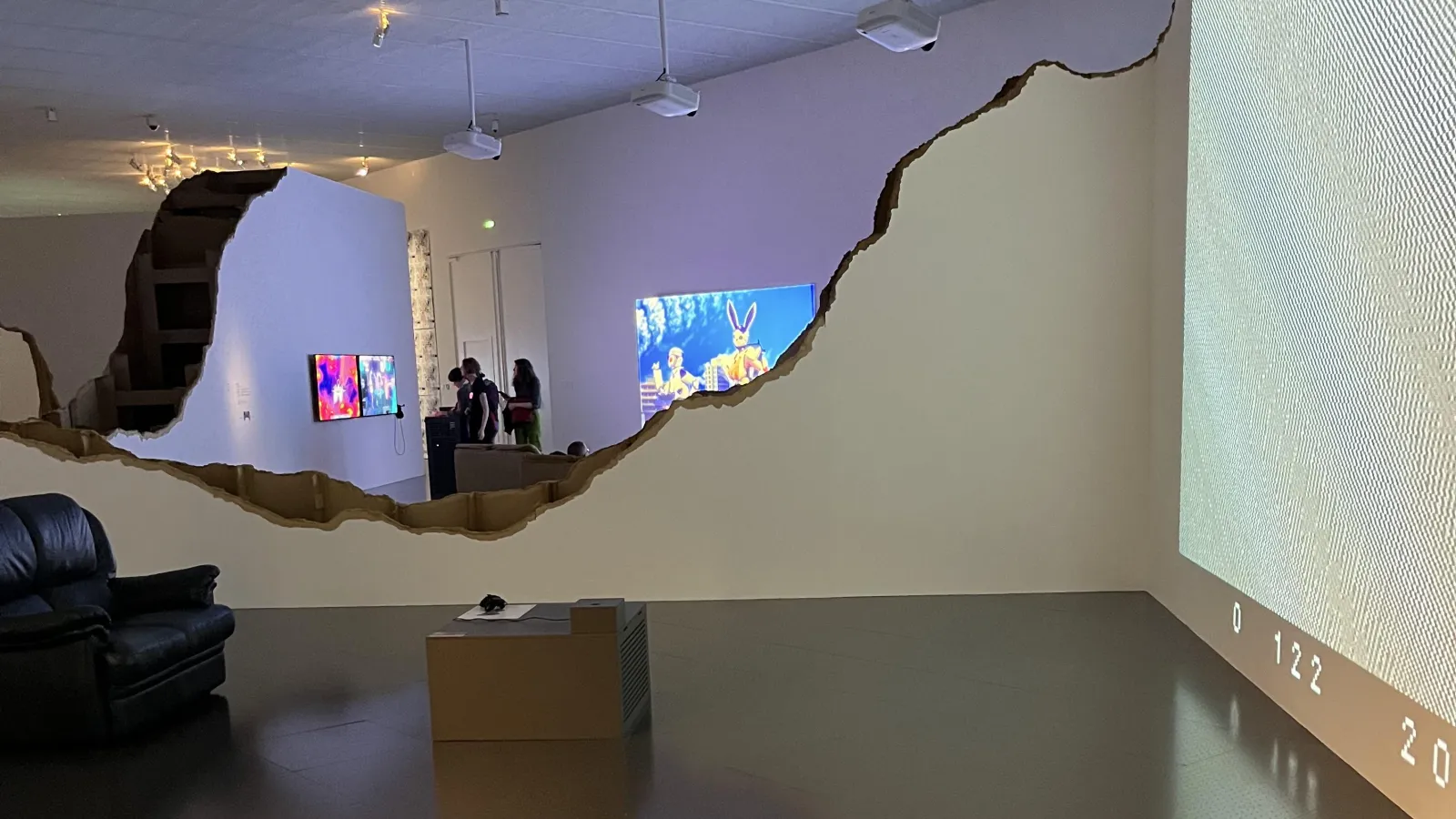 A gallery space with a scalloped wall and video screens