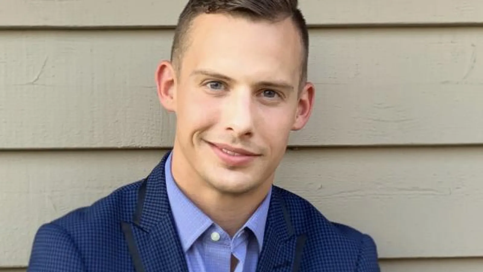 Clayton Kindred against a white wall wearing a blue suit