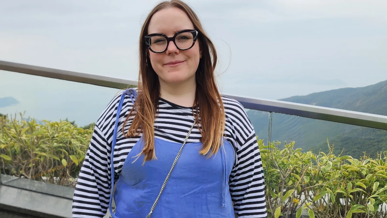 April Riddle Standing outside wearing a blue overall dress and stripped shirt.