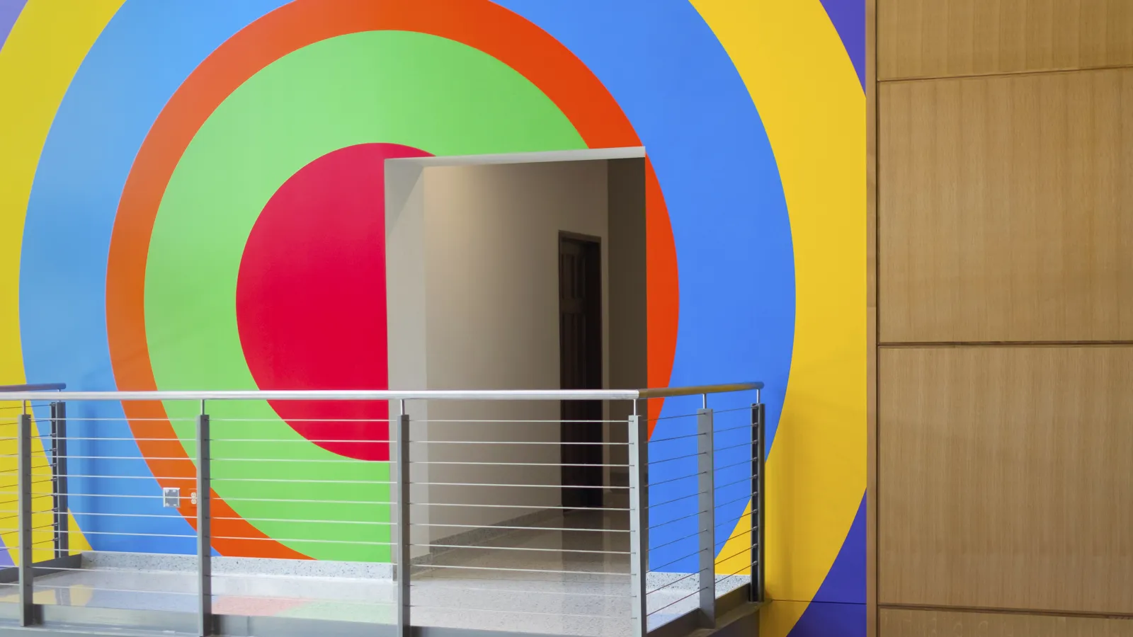 An image of a doorway and viewing balcony with a colorful, geometric mural by the artist Sol LeWitt painted on the wall behind.
