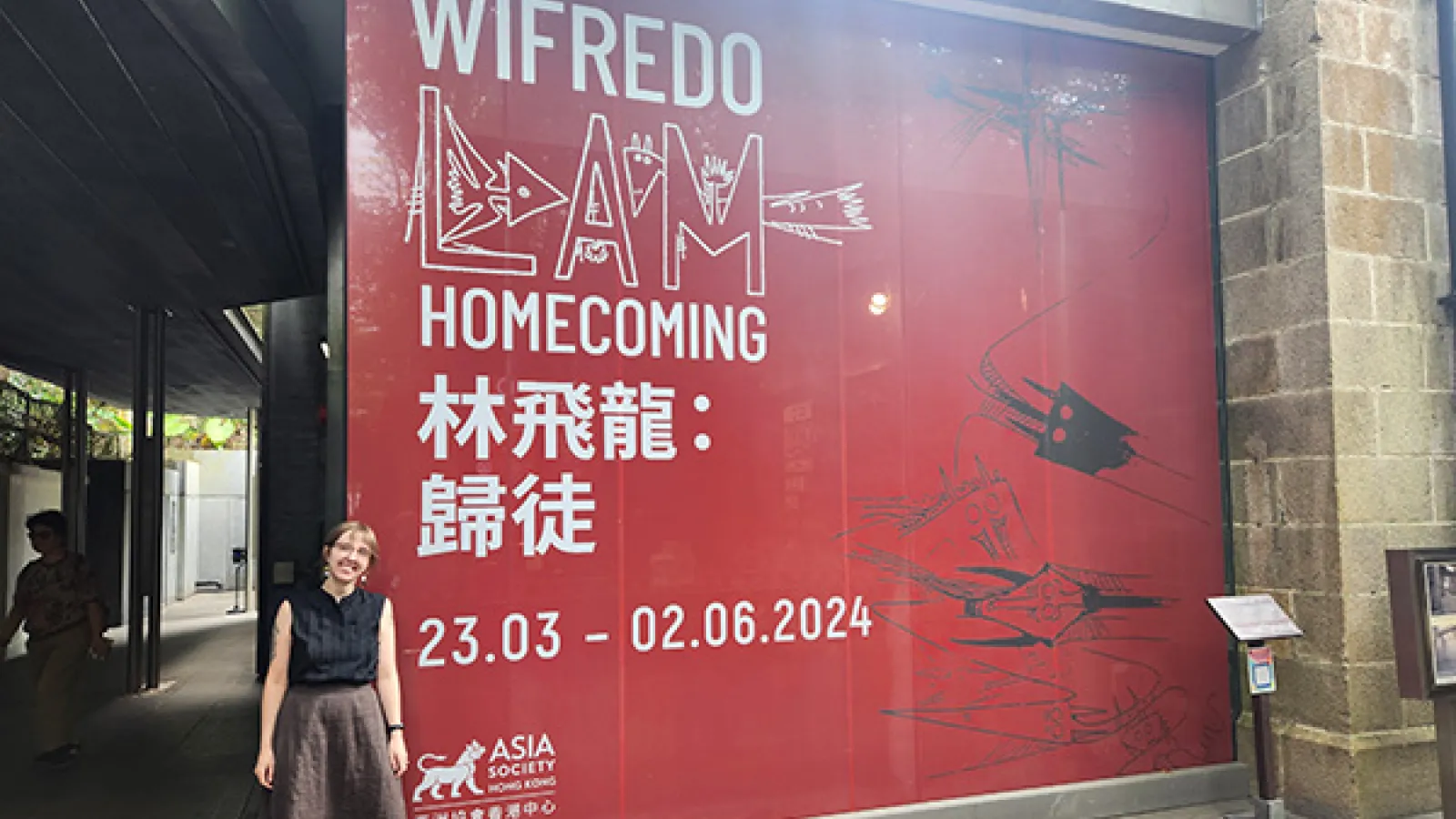 PhD candidate Allie Mickle stands next to a sign for the exhibition Wilfredo Lam: Homecoming