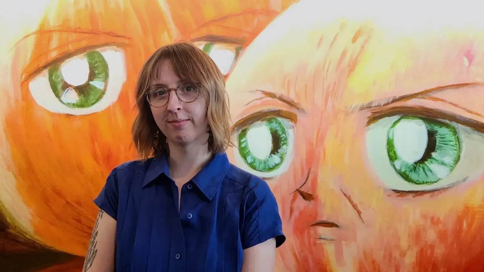 Allie Mickle headshot in front of orange painting with green eyes