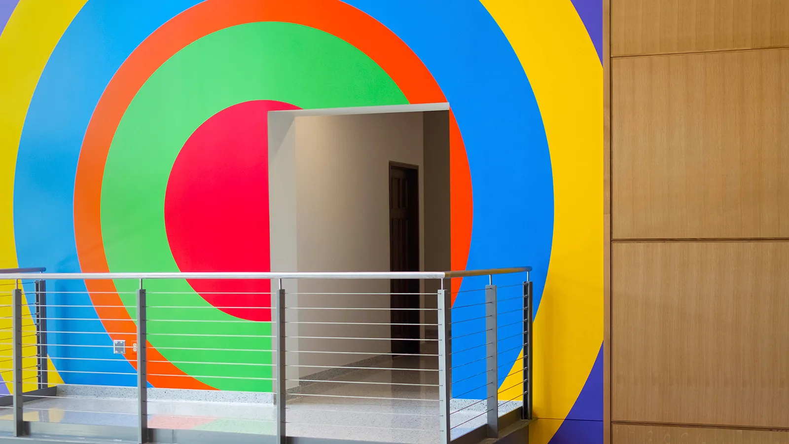 A building interior showing a doorway and balcony with a colorful, geometric mural by the artist Sol LeWitt painted on the wall behind.