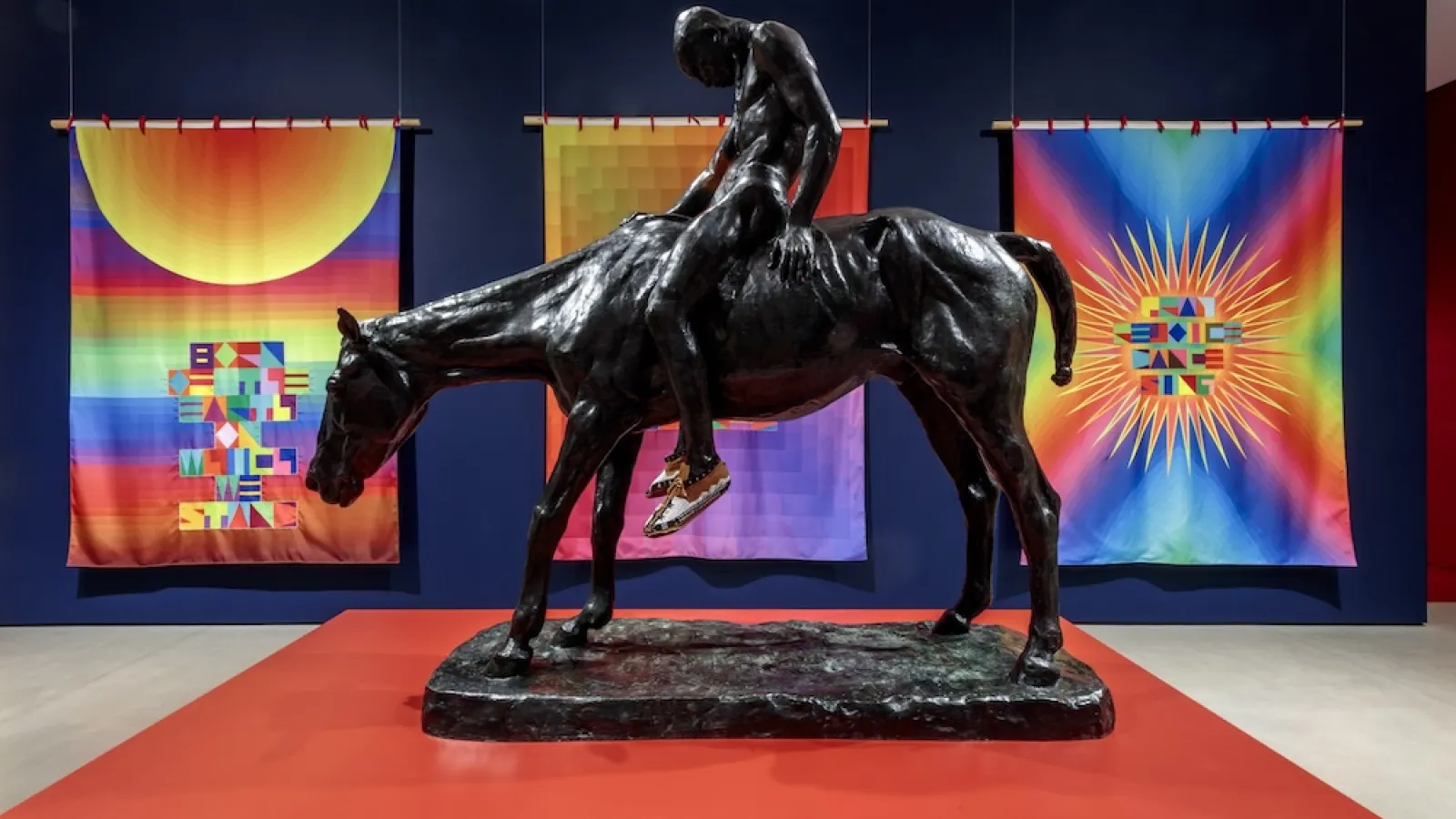 statue of a man riding a horse in front of bright tapestries