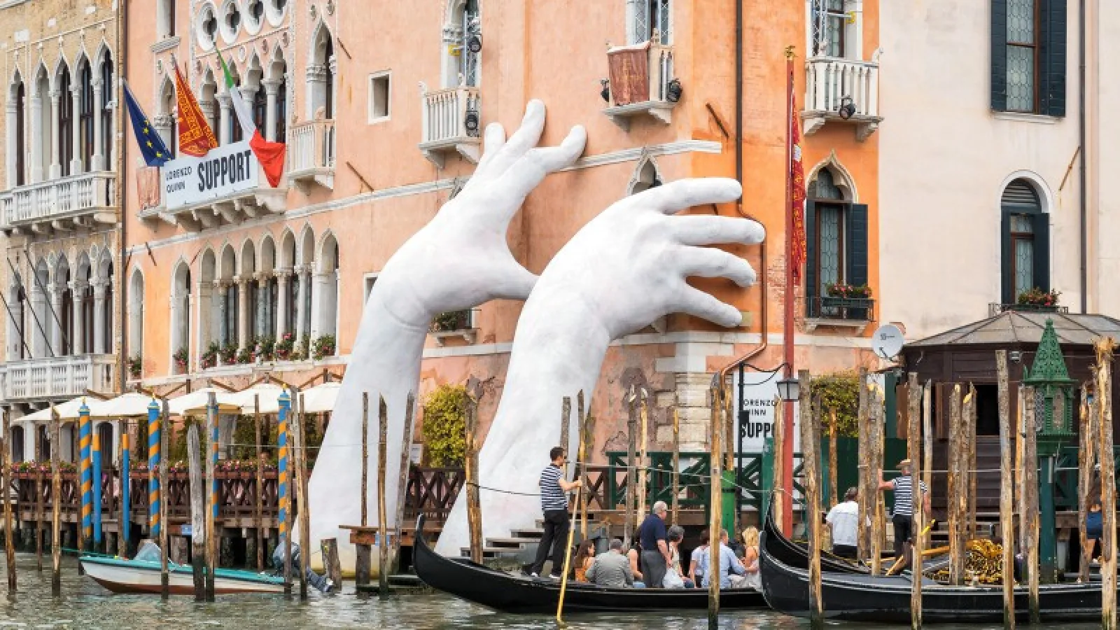 White hand statues holding up a venetian building over the river