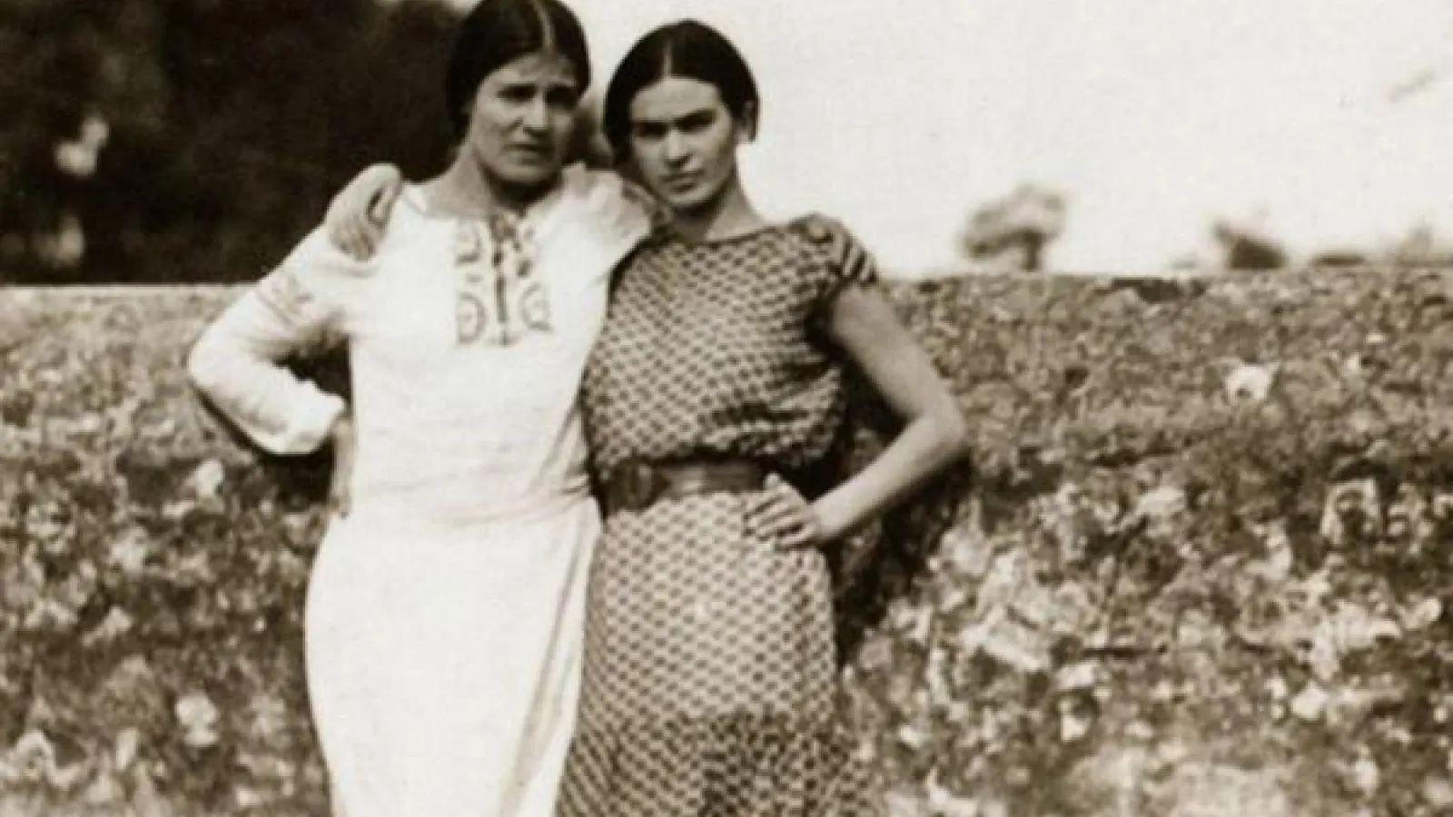 Frida Kahlo and Tina Modotti with arms around each other in front of wall