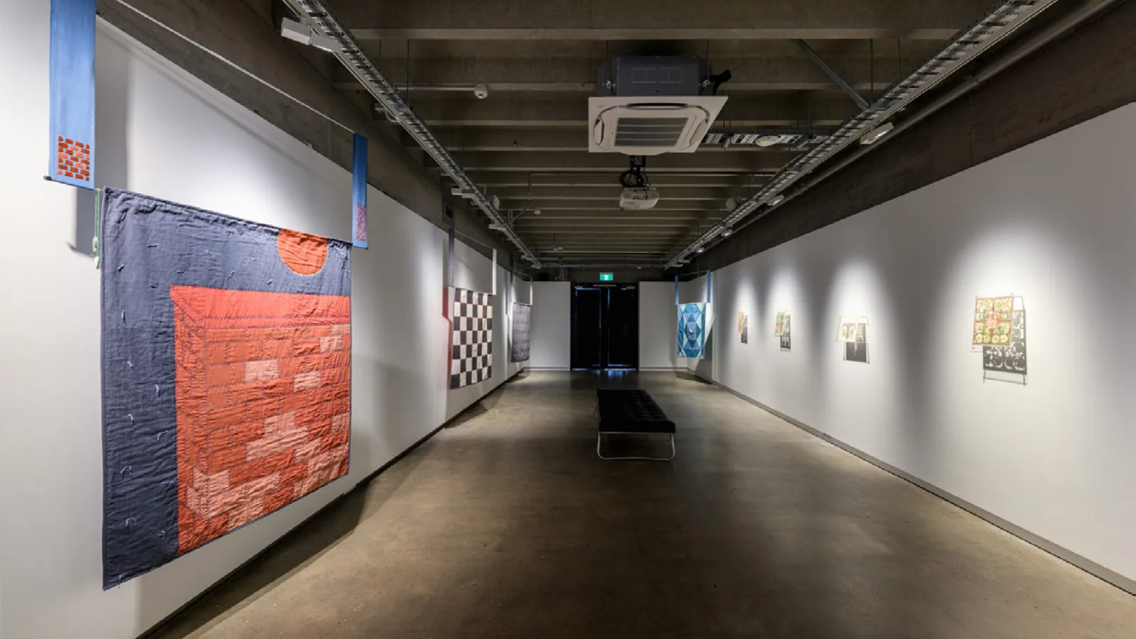 A white room with a checkered floor and a large blue and red textile hanging on the wall.