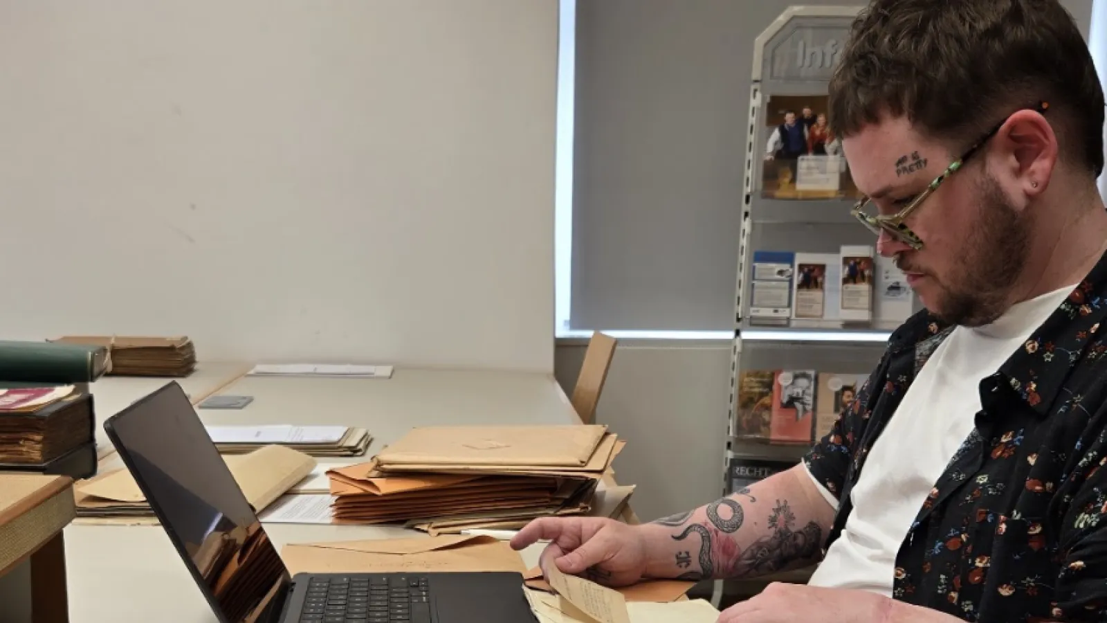 Cole Graham researching at a computer, surrounded by papers.