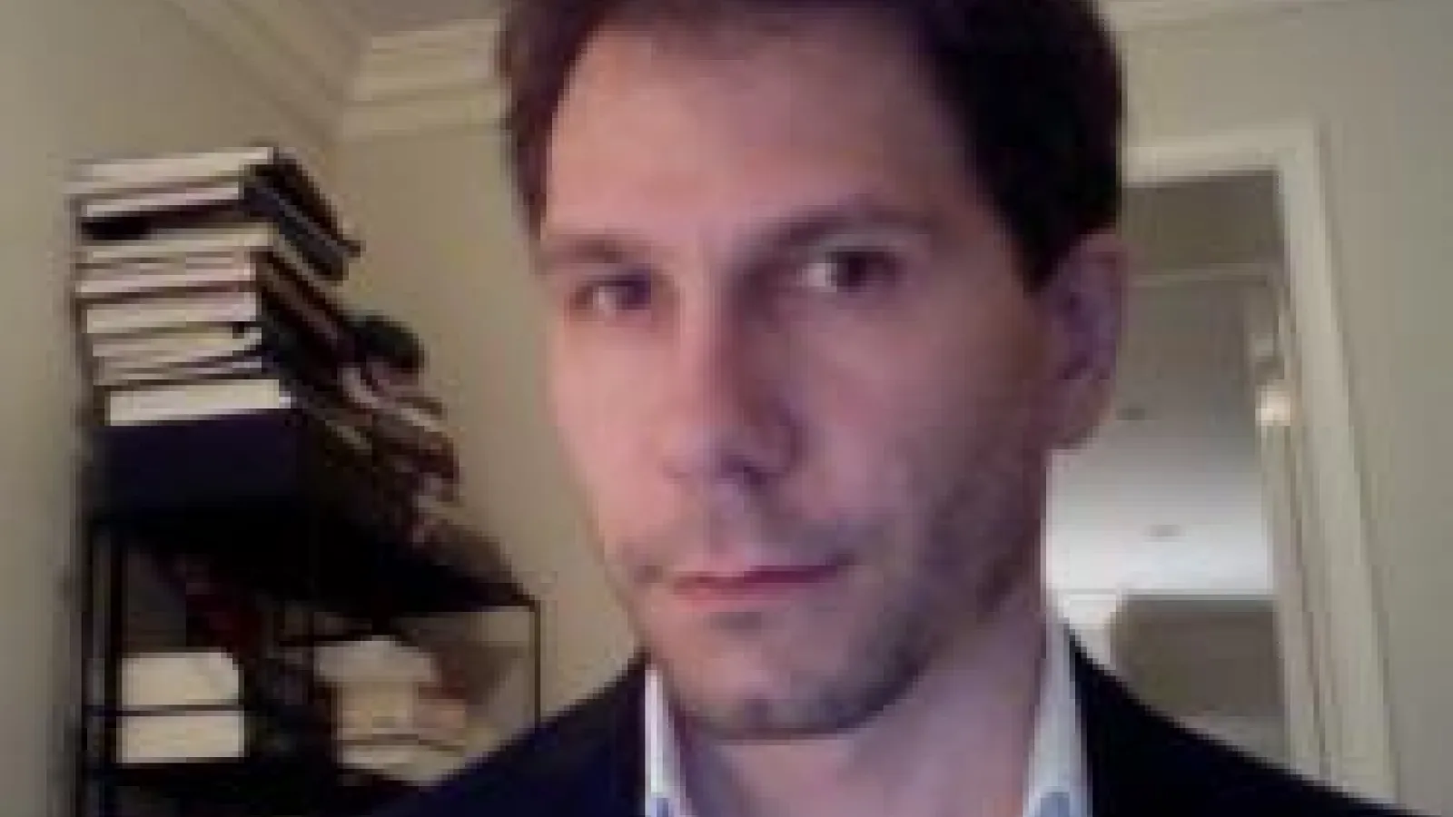 Christian Kleinbub wearing a black suit jacket and white button down shirt in front of a book shelf