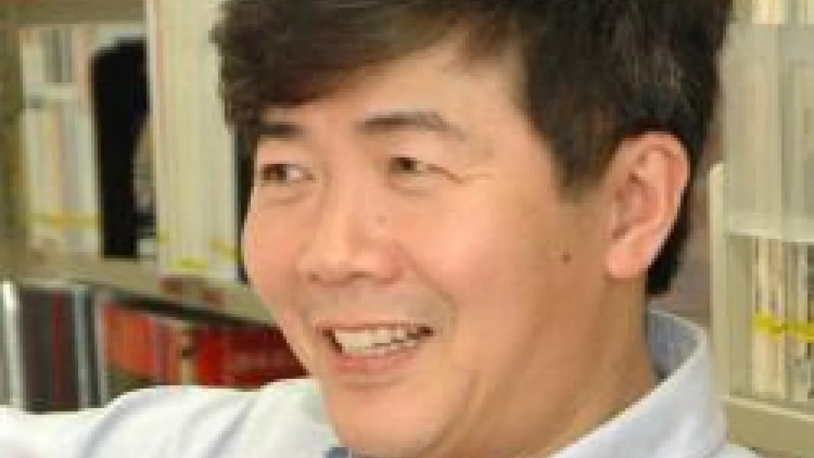 Kuiyi Shen wearing a white button down shirt standing in front of a book shelf.