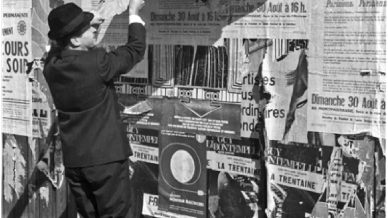 A man peeling a strip of advertisements from an outdoor wall