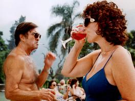 film still of woman in swimsuit sipping drink and man smoking