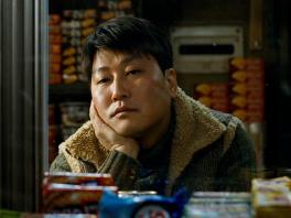 still from the movie the host - depicts person pensively looking off with head cradled in hand. food items on shelves as in a store visible in background and foreground.