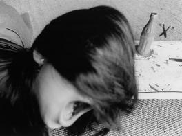 black and white photograph of person's head - half of face is obscured by long hair and the only part visible is a wide open mouth and half of the ear.