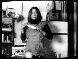 blurry black and white television screen image of figure holding knife in what appears to be a kitchen