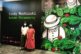 Two women, both wearing masks, stand in front of a dark wall under the title "Cindy Mochizuki: Autumn Strawberry"