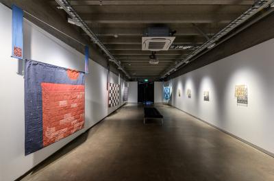 A white room with a checkered floor and a large blue and red textile hanging on the wall.