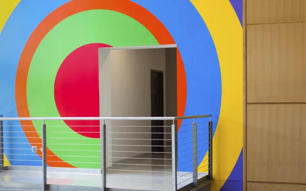An image of a doorway and viewing balcony with a colorful, geometric mural by the artist Sol LeWitt painted on the wall behind.