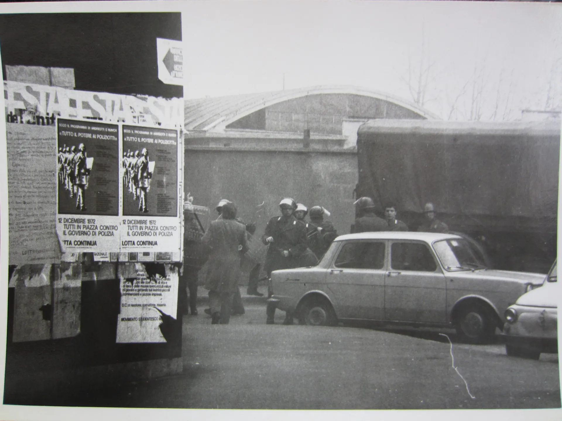 black and white scene of car, police and protest flyers on board in foregrounduova sinistra Marco Pezzi (Marco Pezzi Archive of the New Left), Bologna, Italy.