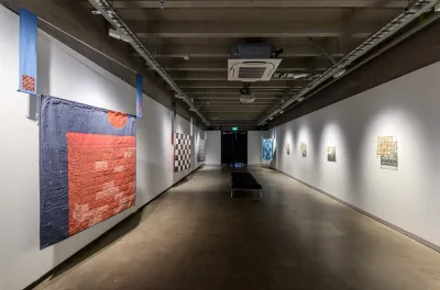 A white room with a checkered floor and a large blue and red textile hanging on the wall.