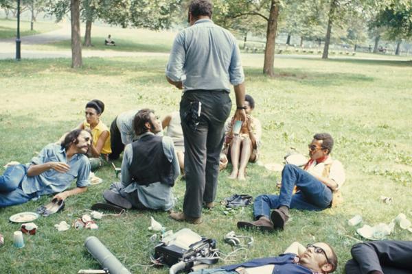 Film still showing group of people sitting talking in grassy field