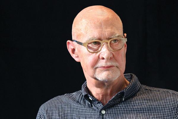 headshot of man with glasses and short white beard on black background