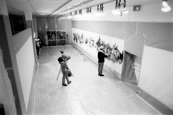 black and white image of a gallery where artist is being filmed