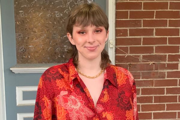 Laurel Hilliard headshot, posing in red shirt in front of brick wall