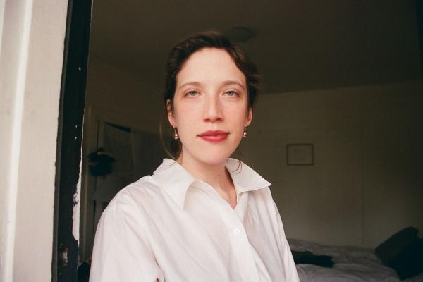 figure in white shirt with light skin, brown hair, and red lips in front of dimly lit room