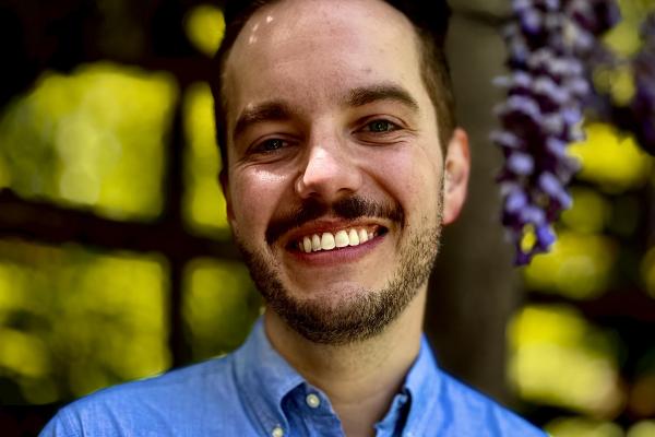 headshot of AJ Meyer, smiling with blue collared shirt against green backgroud