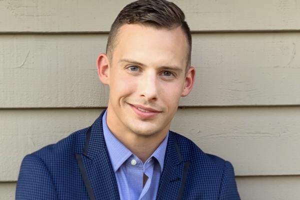 Clayton Kindred against a white wall wearing a blue suit