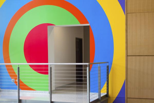 An image of a doorway and viewing balcony with a colorful, geometric mural by the artist Sol LeWitt painted on the wall behind.