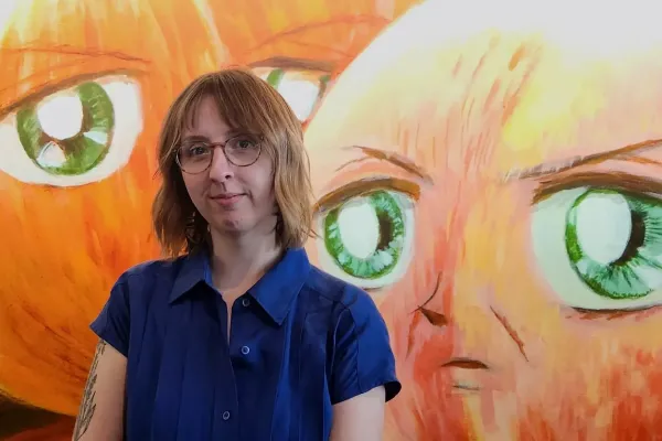 Allie Mickle headshot in front of orange painting with green eyes