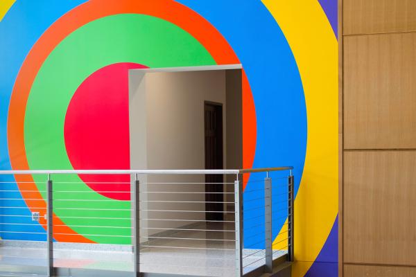A building interior showing a doorway and balcony with a colorful, geometric mural by the artist Sol LeWitt painted on the wall behind.