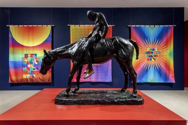 statue of a man riding a horse in front of bright tapestries