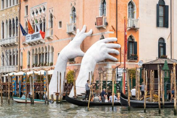 White hand statues holding up a venetian building over the river
