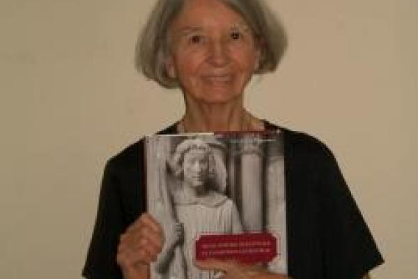 Anne Morganstern wearing black and holding a book in front of a tan wall