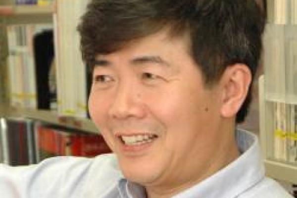 Kuiyi Shen wearing a white button down shirt standing in front of a book shelf.