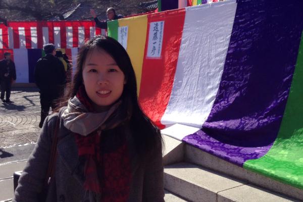 Yanfei Yin standing outside in front of colorful fabrics 