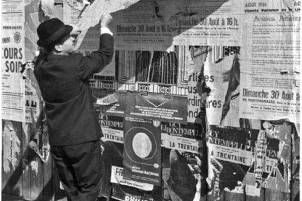 A man peeling a strip of advertisements from an outdoor wall