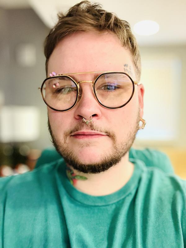 PhD Candidate, Cole Graham wearing a turquoise top and black rim glasses