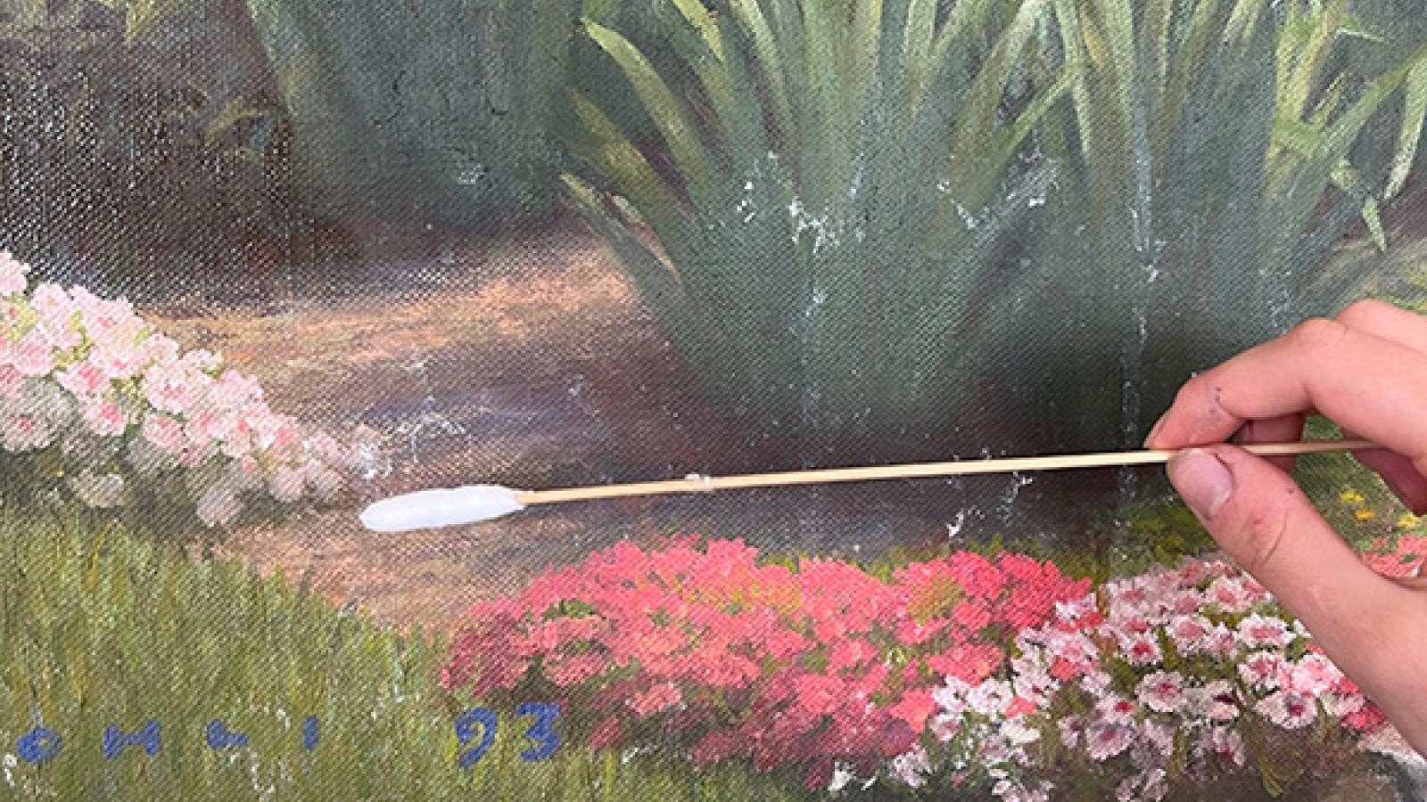A detail of the restoration process in which the painting is being treated with a cotton swab