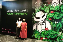 Two women, both wearing masks, stand in front of a dark wall under the title "Cindy Mochizuki: Autumn Strawberry"