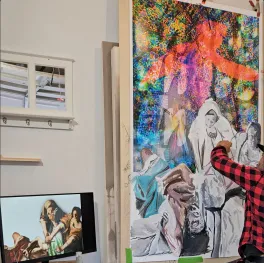 A man painting on a large colorful canvas.